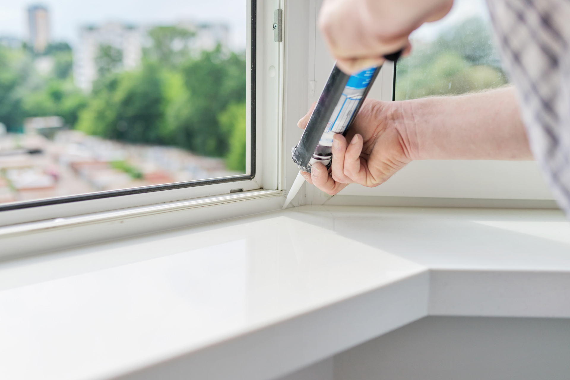 Worker with construction syringe fills seam between sill and window with silicone sealant